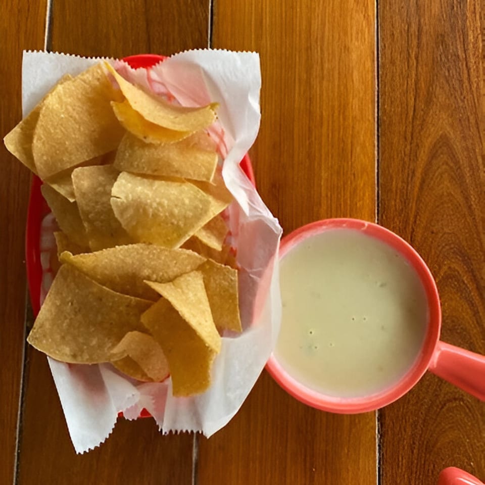 A red basket of Krave Tacos tortilla chips and a side of queso dip on a wooden table.