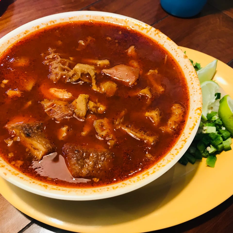 A bowl of Krave Tacos' menudo, a rich red Mexican soup with tripe, served with lime and jalapeños.