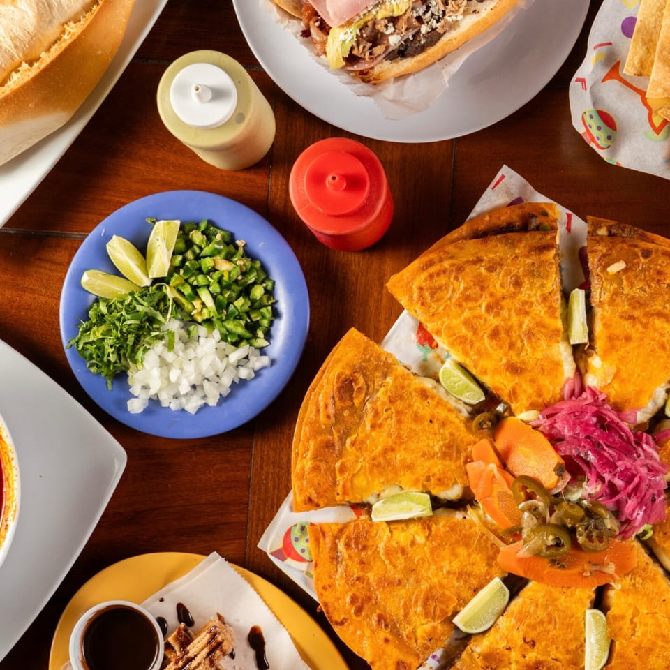 A vibrant spread of Krave Tacos' Mexican dishes, including a large quesadilla, fresh toppings, and churros.